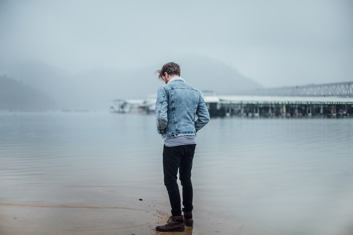 Man in denim jacket by the foggy water