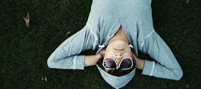 Person in hoodie and sunglasses lying on grass