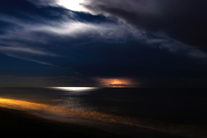 Lightning storm over the ocean at night with moon reflection