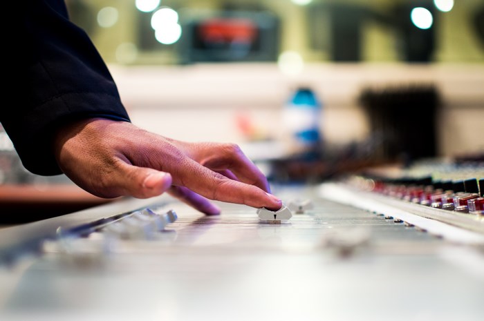 Hand adjusting sliders on a sound mixer board