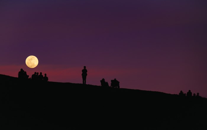 People silhouetted on a hill watching the full moon rise