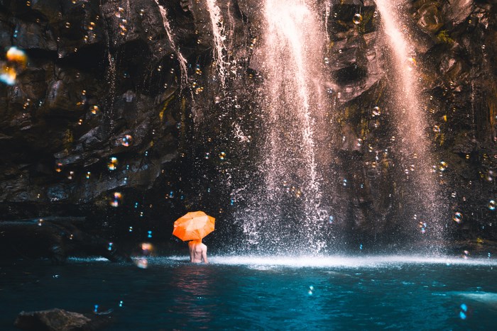Person with orange umbrella under a waterfall