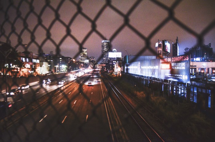 Night highway traffic and city skyline through a fence