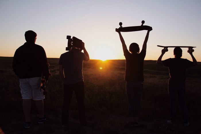 Four friends with skateboards at sunset