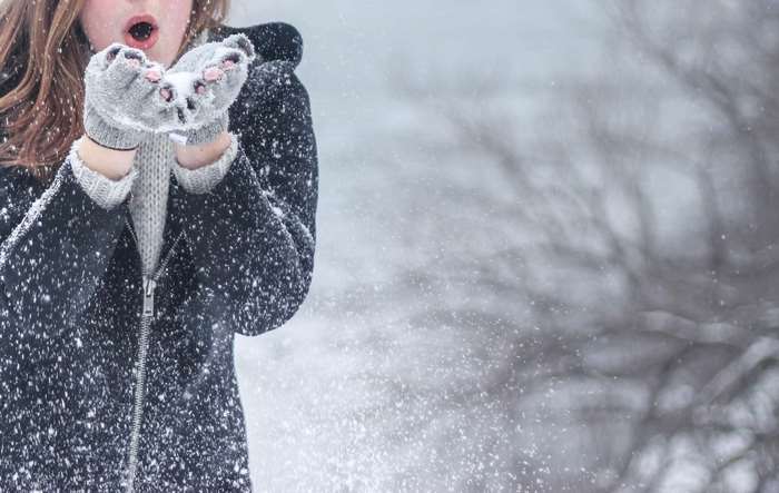 Woman blowing snow from her hands in winter