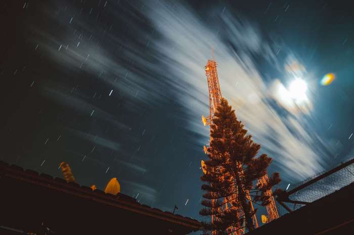 Long exposure night sky with stars and clouds over a cell tower