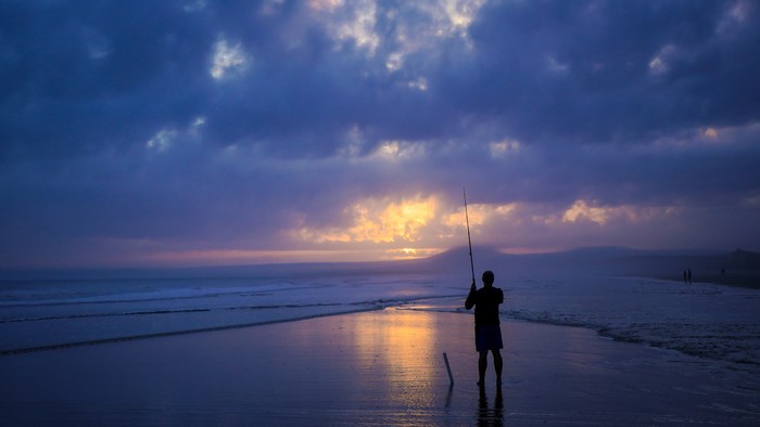 Fisherman casting a line on a beach at sunset