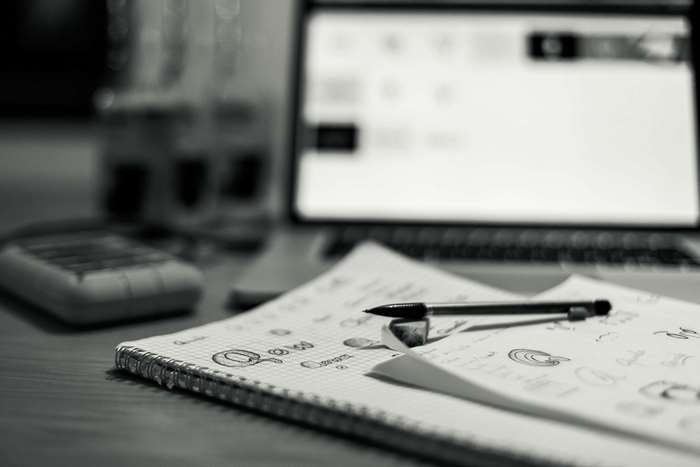 Notebook with sketches and pen on a desk with laptop