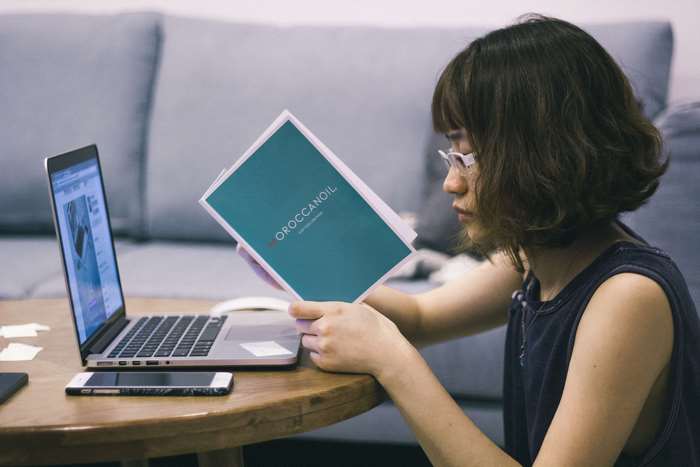 Woman reading a book next to a laptop and iPhone