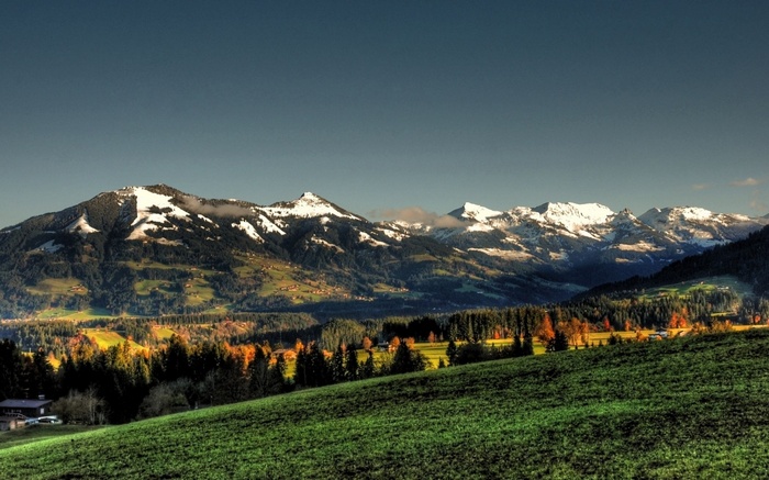 Snow-capped mountains and a green valley with autumn trees