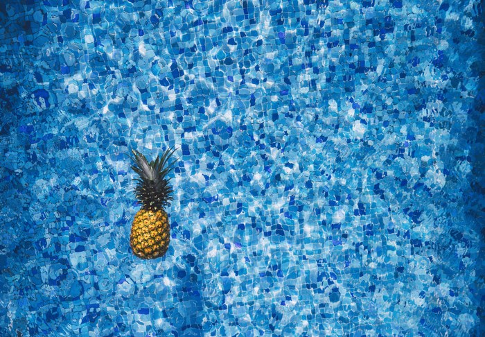 Pineapple floating in a blue tiled swimming pool