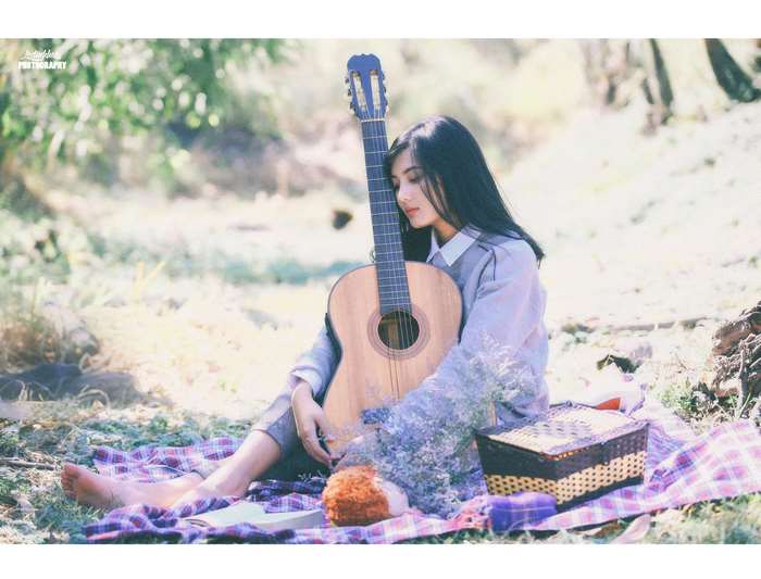 Young woman with guitar sitting outdoors