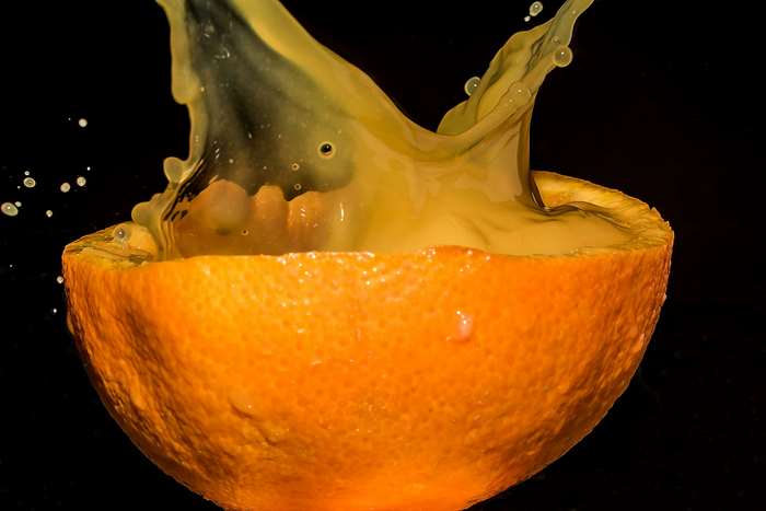 Orange juice splashing out of half an orange