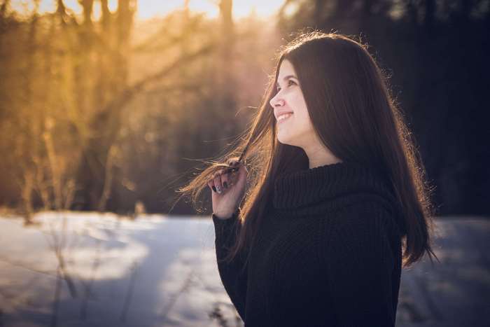 Young woman smiling in a snowy forest at sunset