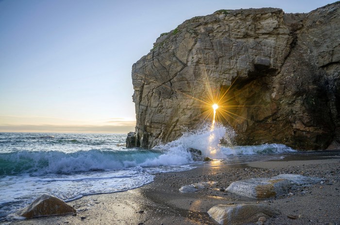 Sunlight shines through a rock arch on a Brittany beach
