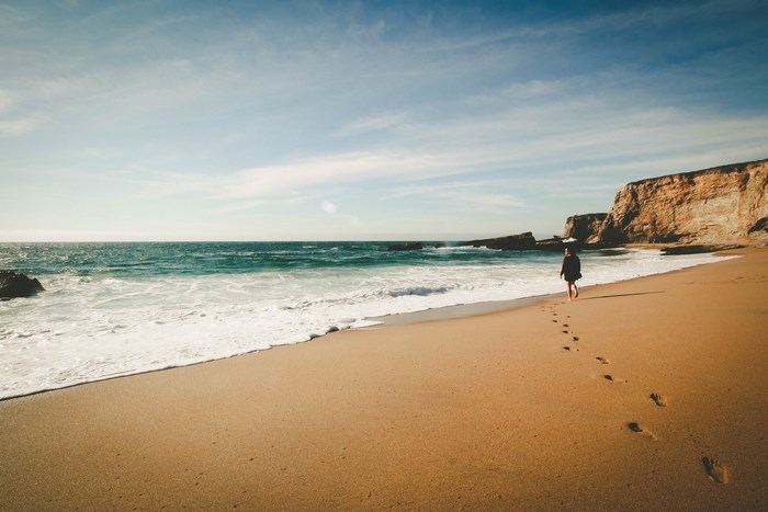 Woman walking on a sandy beach with cliffs