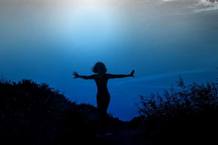 Silhouette of a woman with arms outstretched against a bright sky
