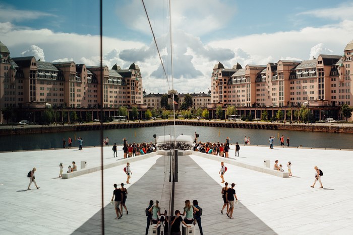 People walking on a waterfront with buildings reflected in glass