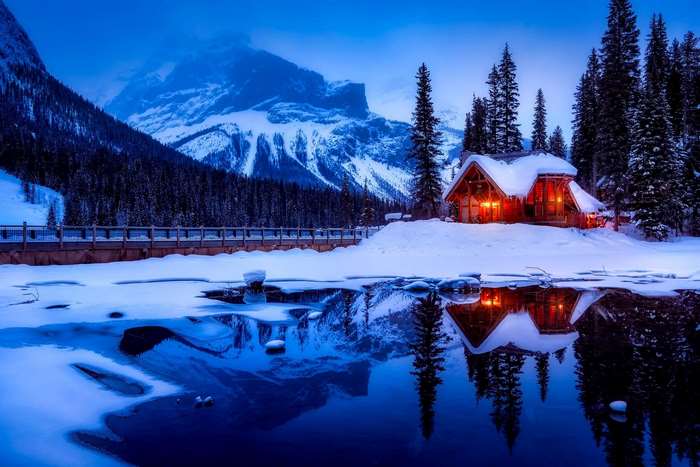 Cozy cabin by a frozen lake with snowy mountains