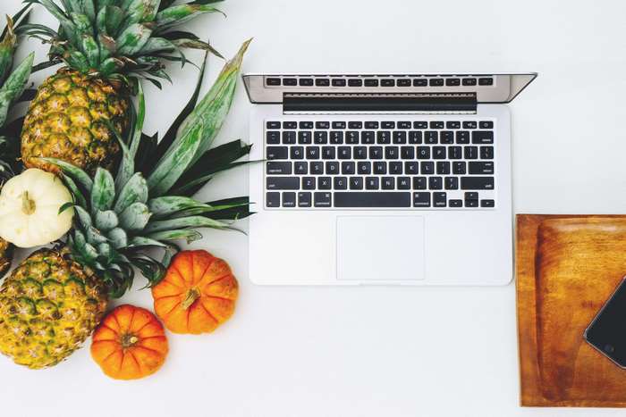 Laptop with pineapples, pumpkins, and a smartphone on a wooden tray