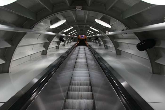 Escalator in a modern tunnel with train in distance