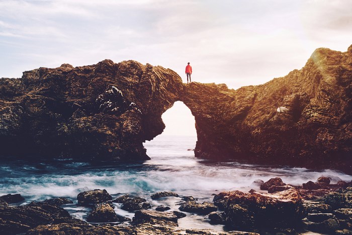 Man standing on a natural rock arch over the sea