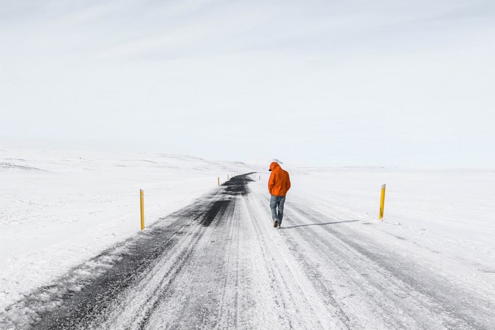 Man in orange jacket walks on snowy road in Iceland