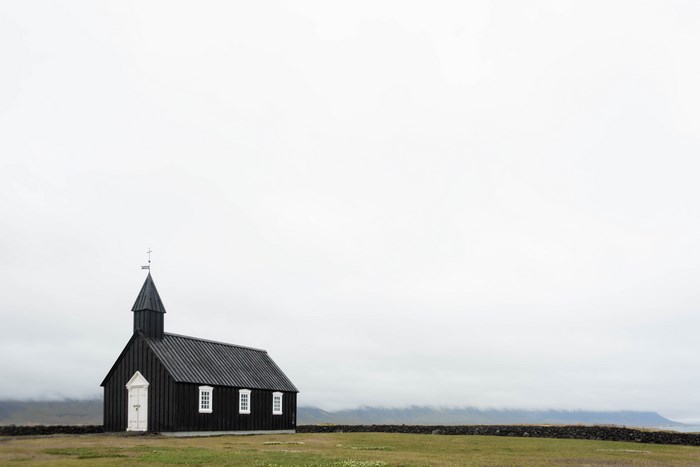 Black church in Iceland with a stone wall and cloudy sky