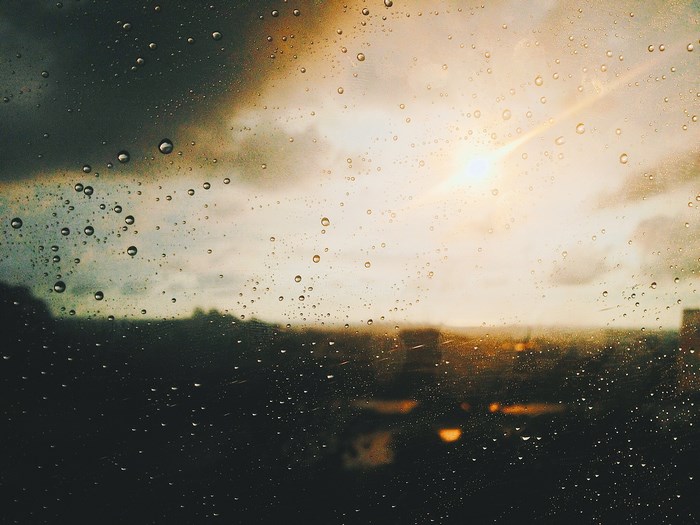 Raindrops on a window with sun flare and city skyline
