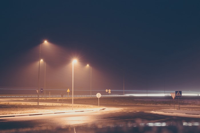 Streetlights illuminate a foggy road at night with signs