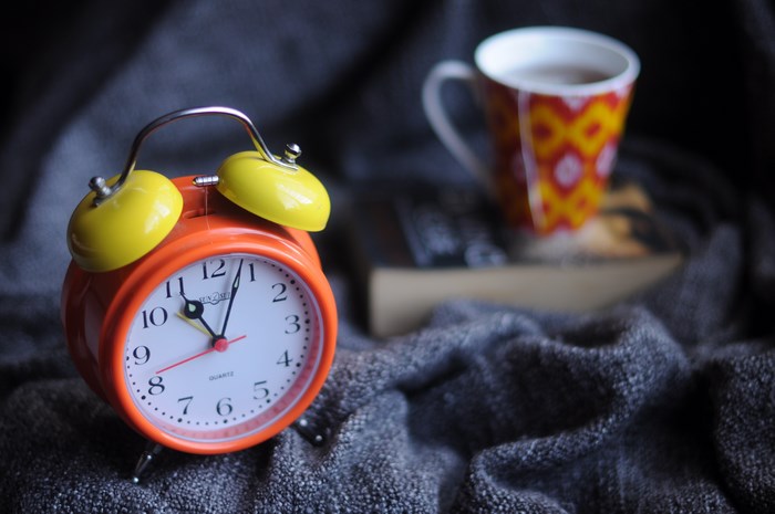Orange alarm clock and cup of tea on blanket