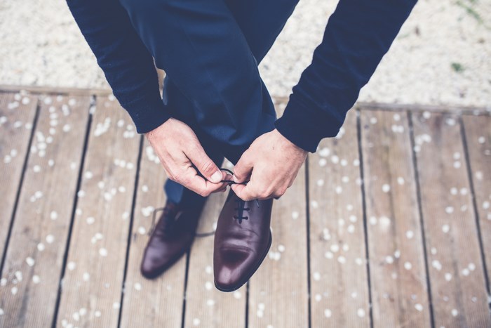Man tying brown leather shoes on wooden deck