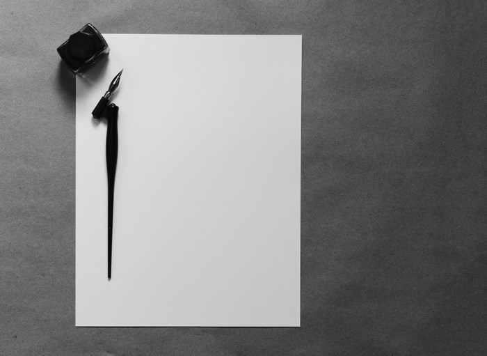 Black ink bottle and calligraphy pen on white paper