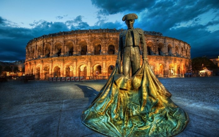 Matador statue in front of Roman amphitheater at dusk