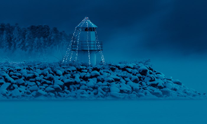 Lighthouse decorated with fairy lights on a snowy rocky shore