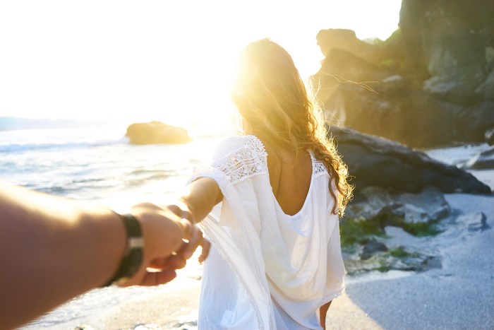 Man holding woman's hand on a beach at sunset