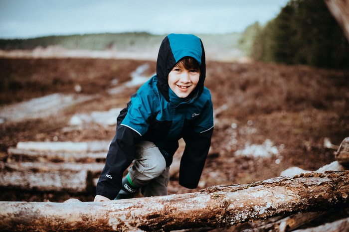 Boy in a blue hoodie climbing over logs