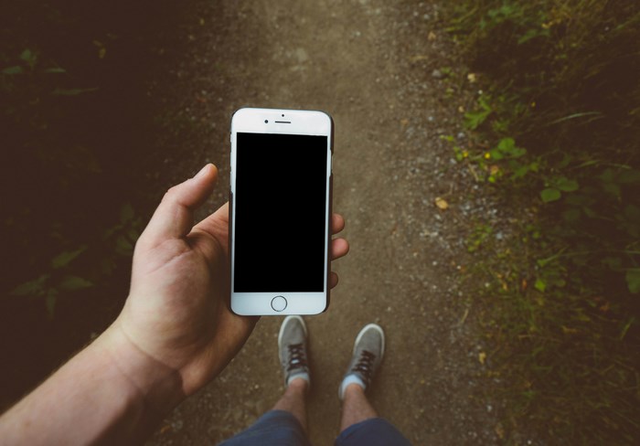 Person holding an iPhone on a dirt path