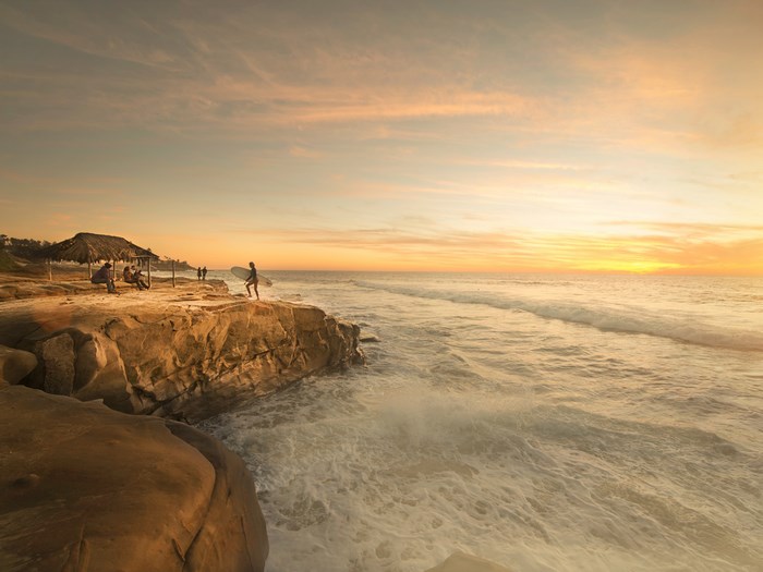 Surfer on cliff overlooking the ocean at sunset in San Diego