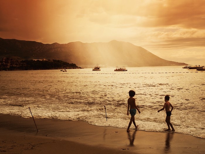 Two children walk on a beach at sunset