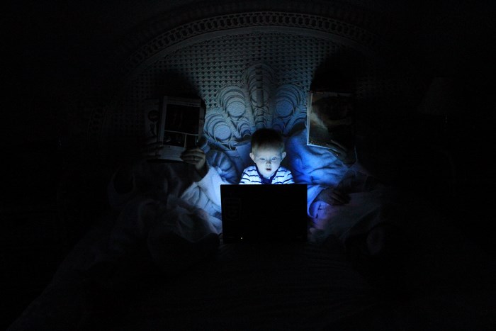 Child and parents looking at a laptop in bed at night