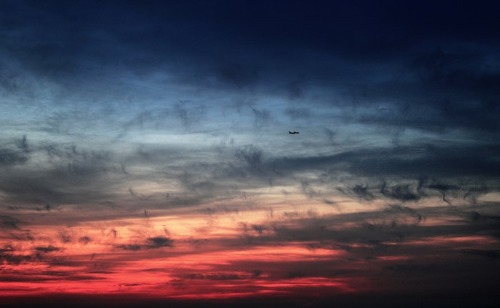 Airplane flying through a colorful sunset sky with clouds