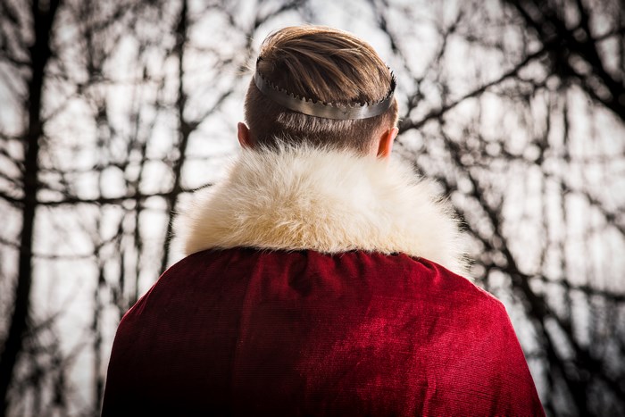 Man wearing a crown and red coat in forest