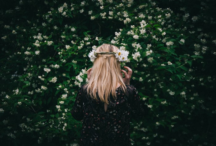 Woman with a floral crown in front of a flowering bush