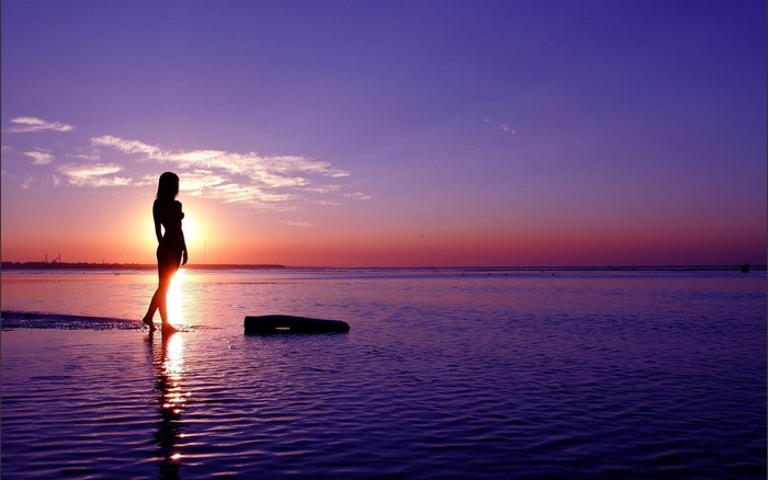 Silhouette of Woman Walking by the Sea at Sunset