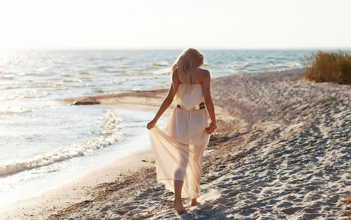 Woman in Flowing Dress Walking on Sandy Beach