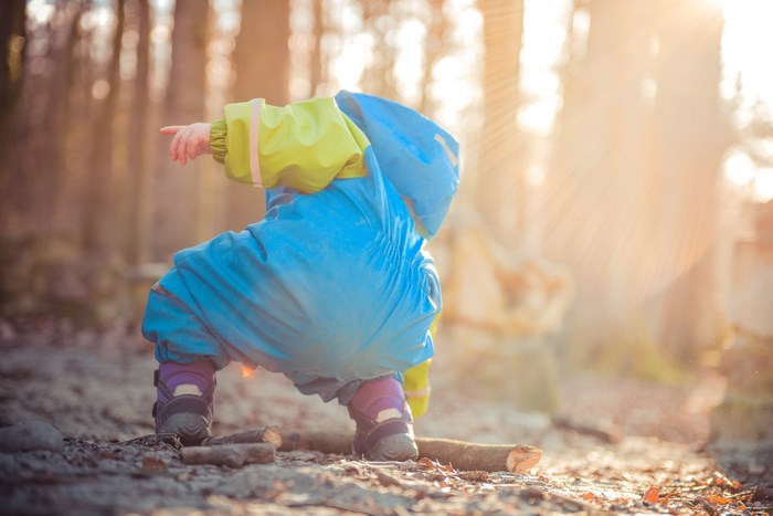 Child in blue raincoat playing in forest