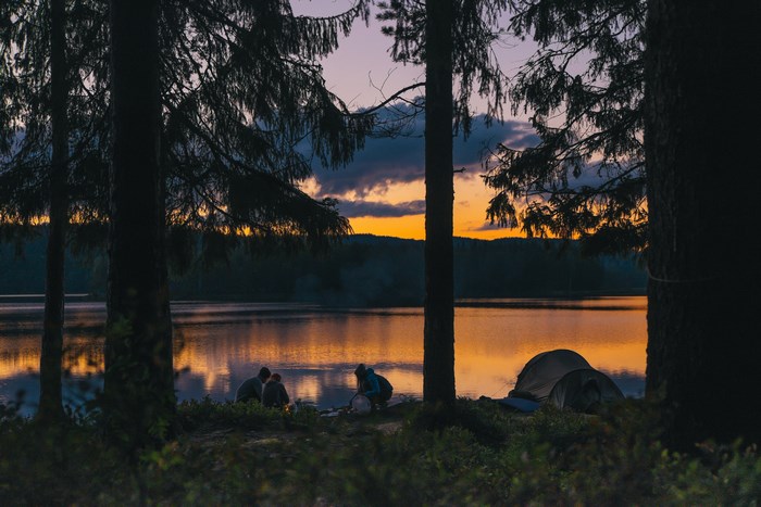 Camping by a lake at sunset with tents and people
