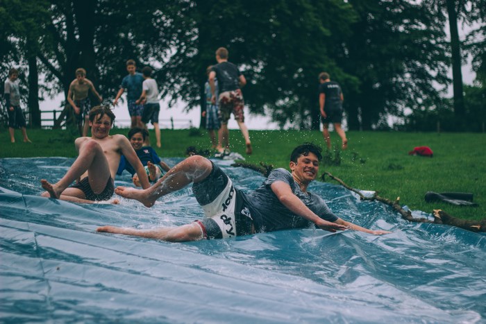 Teens slip and slide on a wet tarp in a grassy park
