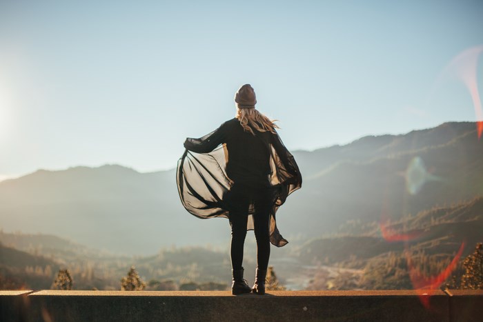 Woman in a black dress and hat on a mountain edge
